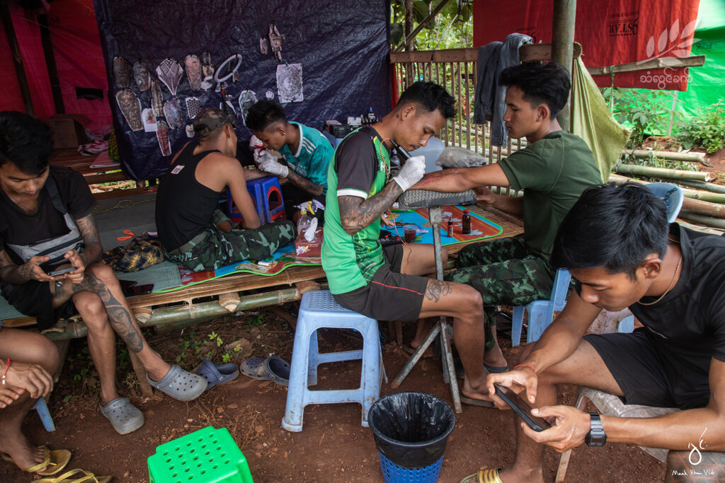 တက်တူးဆိုတဲ့ရေစီးကြောင်းကို တချို့လူငယ်တွေက စွဲမက်ခုံမင်ကြပါတယ်။မြို့ပြနဲ့ ဝေးကွာနေတဲ့ တော်လှန်ရေးရဲဘော်တွေအတွက်တော့ အားလပ်ချိန်လေးမှာ တက်တူးလေးထိုးဖို့ စိတ်ကူးကြတယ်။

အင်တာနက်ပေါ်က ပုံလေးတွေကို ရှာ၊ လွတ်မြောက်နယ်မြေထဲက တက်တူးဆိုင်လေးဆီသွားပြီး ပုံဖော်လေ့ရှိကြပါတယ်။

August 2022 _ Mauk Kham Wah 